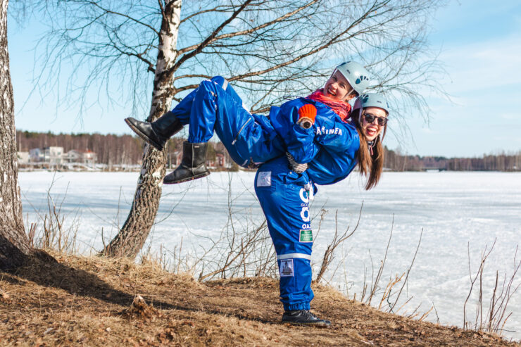 Kaksi kestävyyskasvatuksen opiskelijaa opiskelijahaalarit päällä Kemijoen rannalla.
