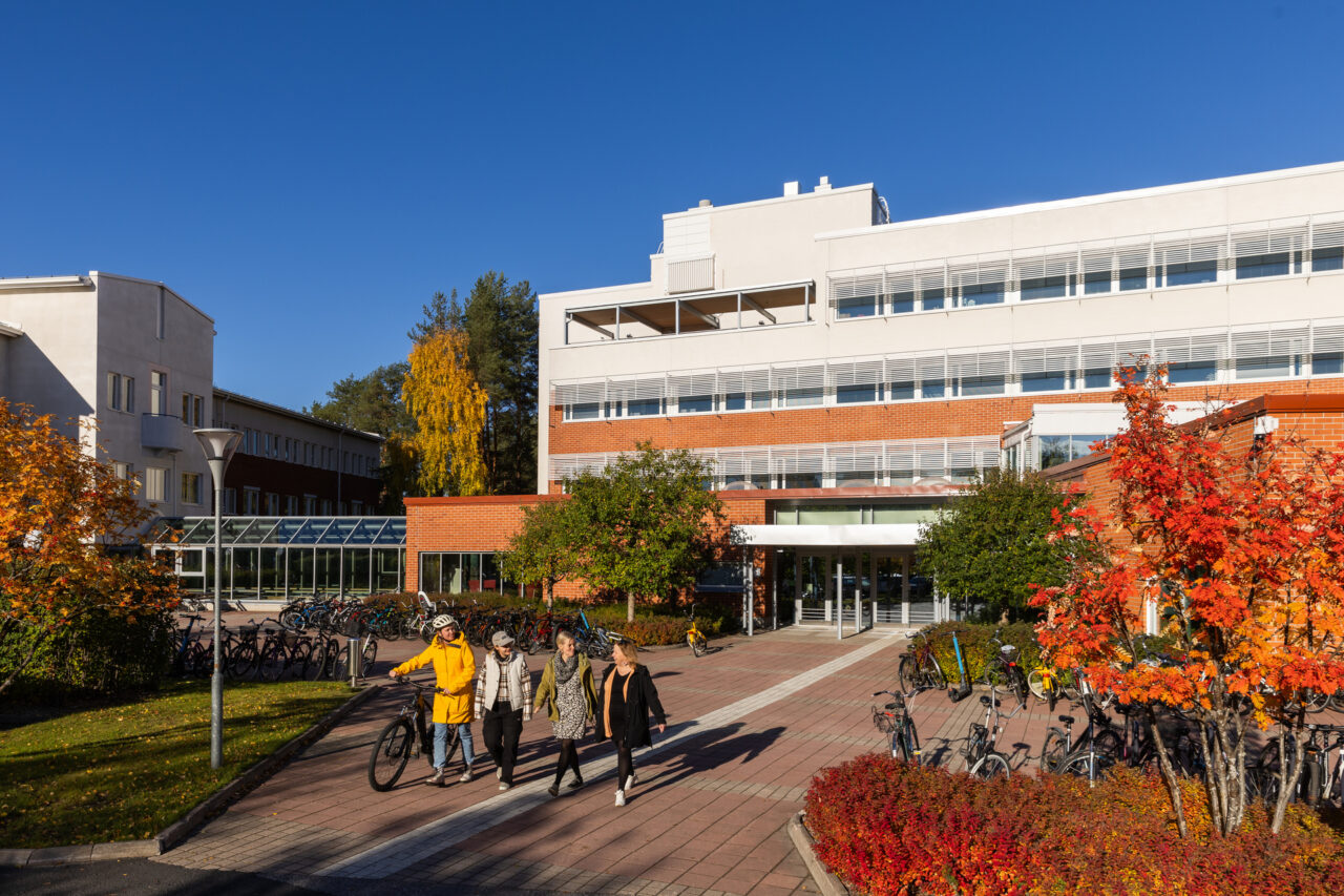 An autumnal photo of the University of Lapland's F-wing. People are walking in the foreground and one of them has a bike.