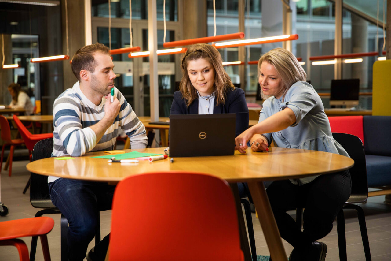 Three employees sit at a wooden table.