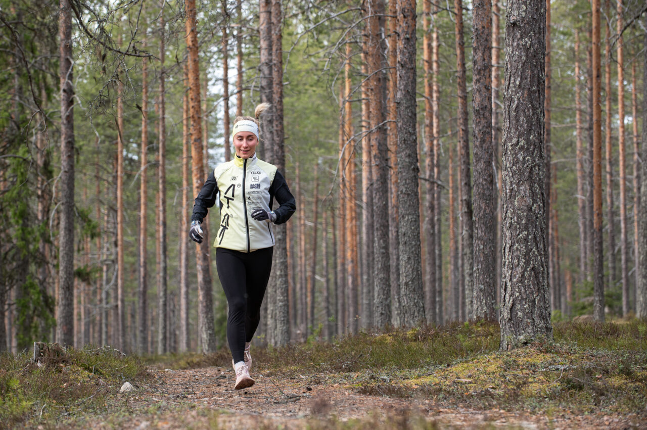 Nainen juoksee mäntymetsässä.
