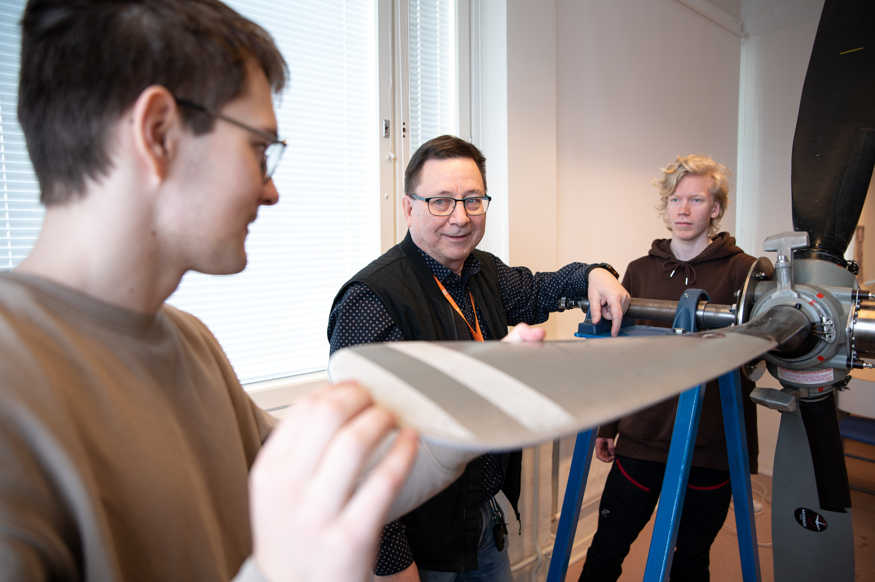 Keski-ikäinen mies kahden nuoren miehen kanssa katsovat lentokoneen rupellia luokkatilassa.